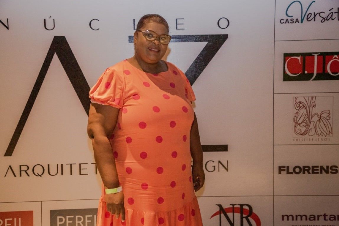 Uma mulher com um vestido de bolinhas está parada em frente a uma parede com logotipos