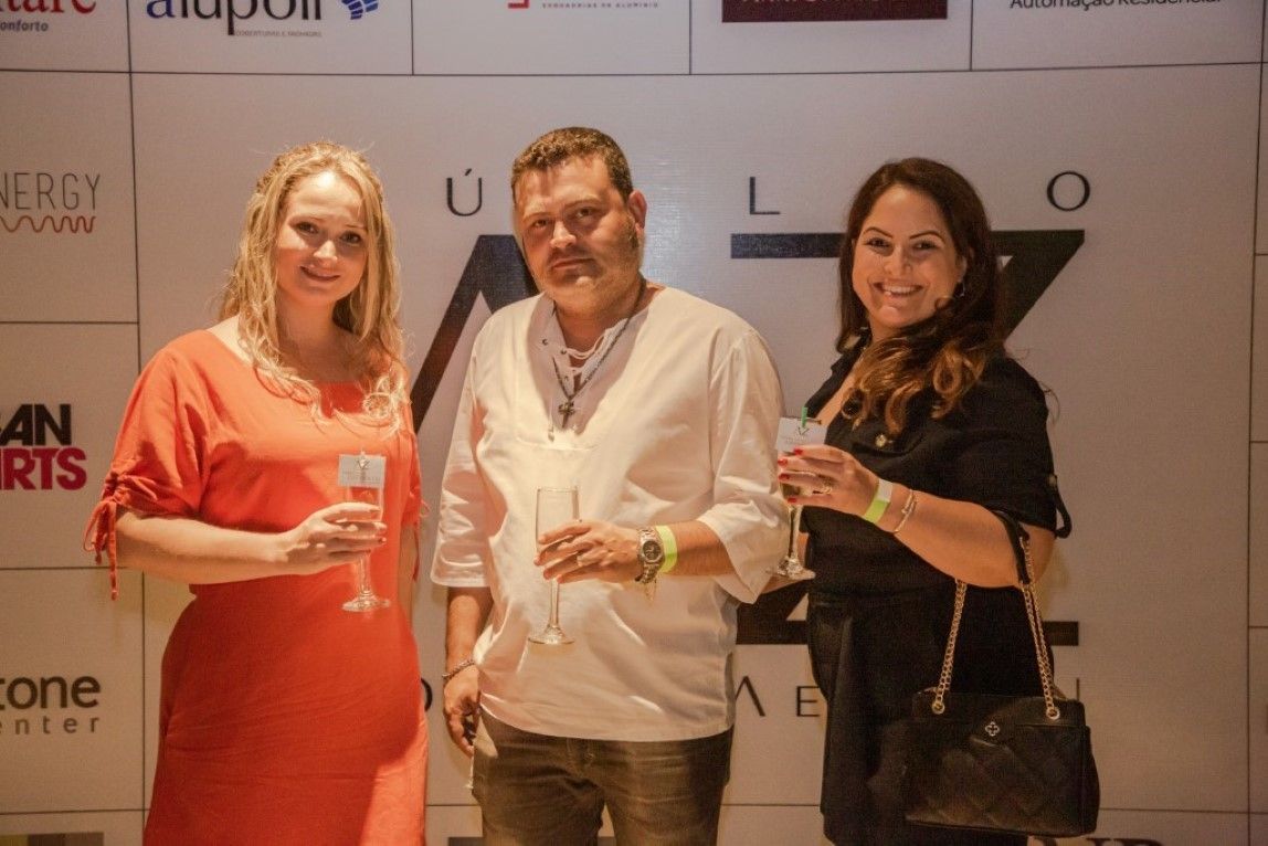 Um homem e duas mulheres estão de pé, um ao lado do outro, segurando taças de vinho.