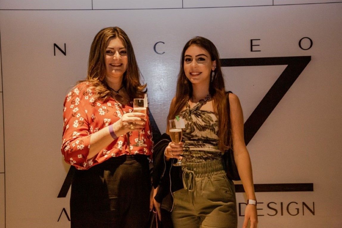 Duas mulheres estão de pé, uma ao lado da outra, em frente a uma placa que diz design.