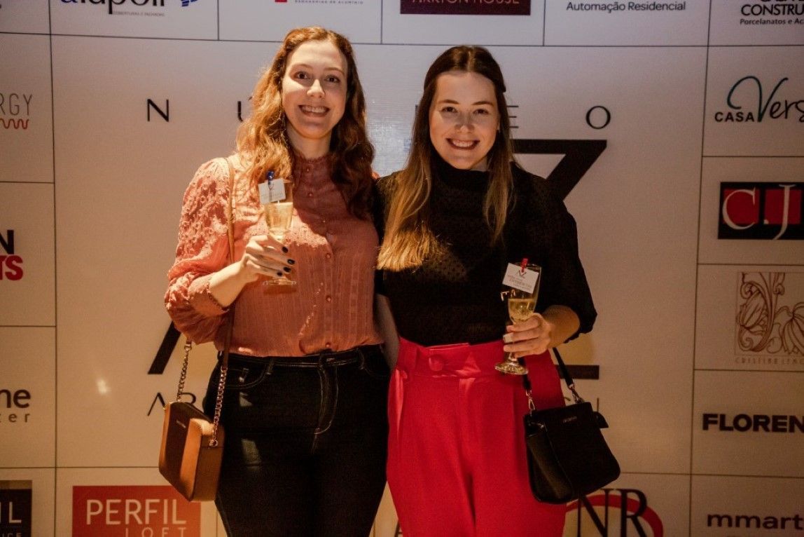 Duas mulheres estão posando para uma foto em frente a uma parede com logotipos.
