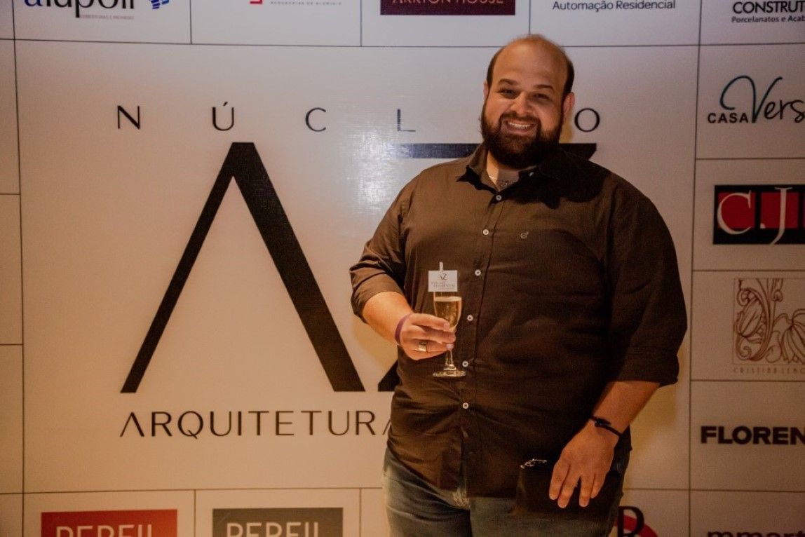Um homem segura uma taça de champanhe em frente a uma placa que diz arquiteto