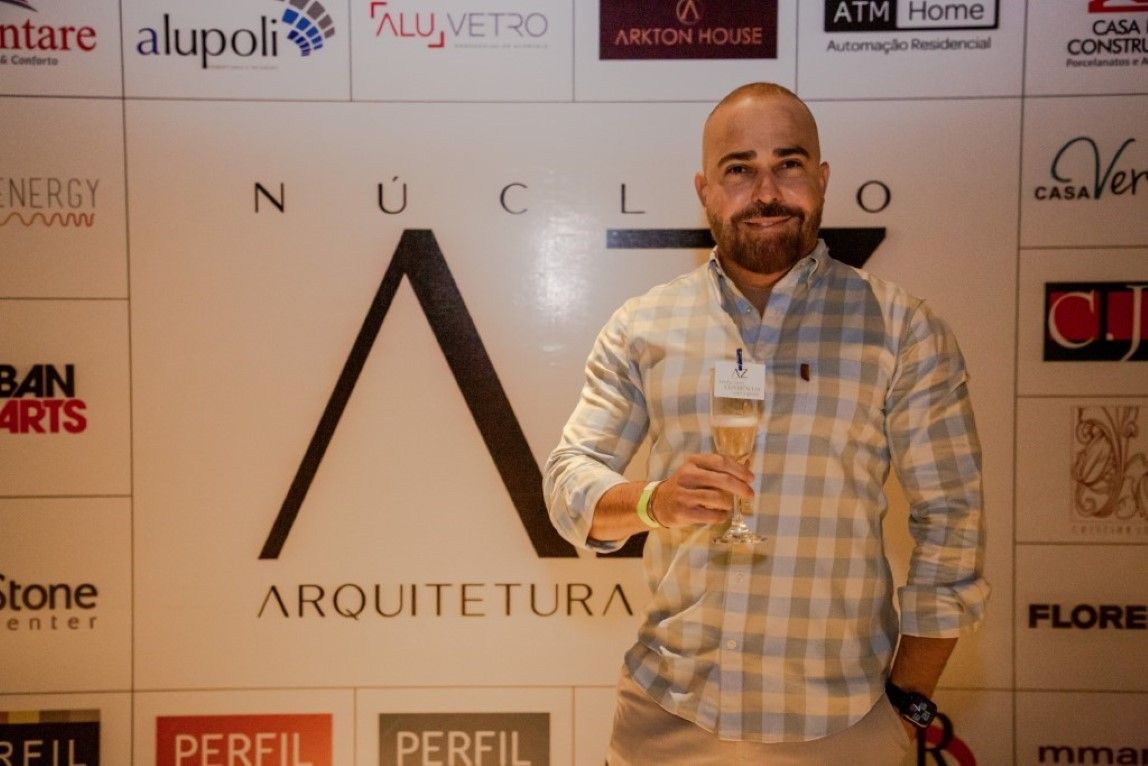 Um homem segura uma taça de champanhe em frente a uma parede com logotipos