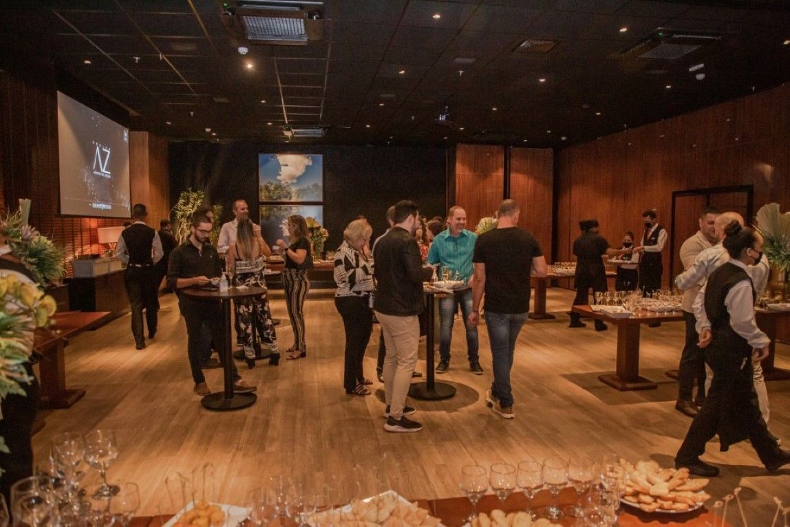 Um grupo de pessoas está de pé ao redor de mesas em uma sala grande.