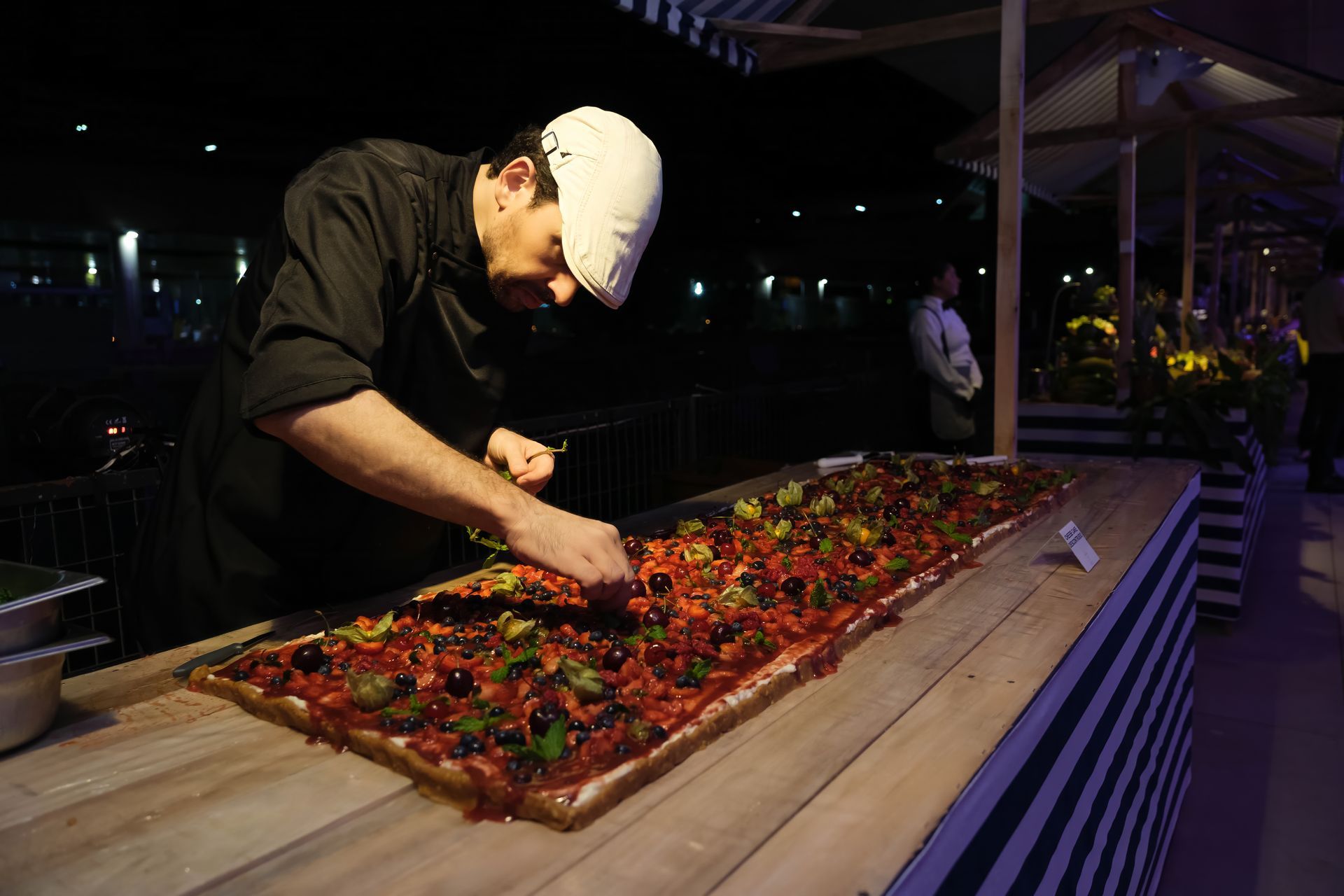Um homem está cortando uma pizza muito longa em uma mesa de madeira.