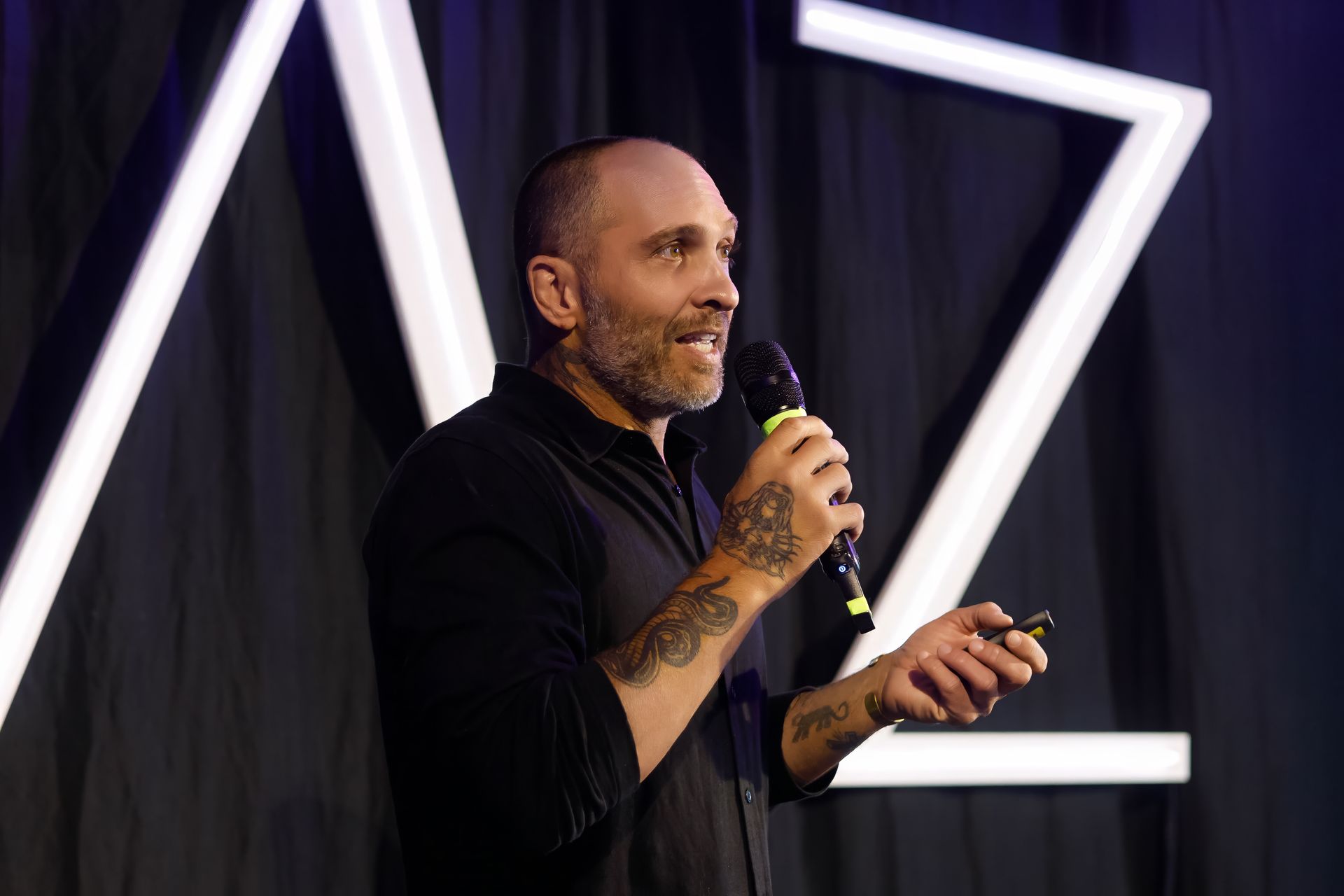 Um homem careca com tatuagens está segurando um microfone e fazendo um discurso.