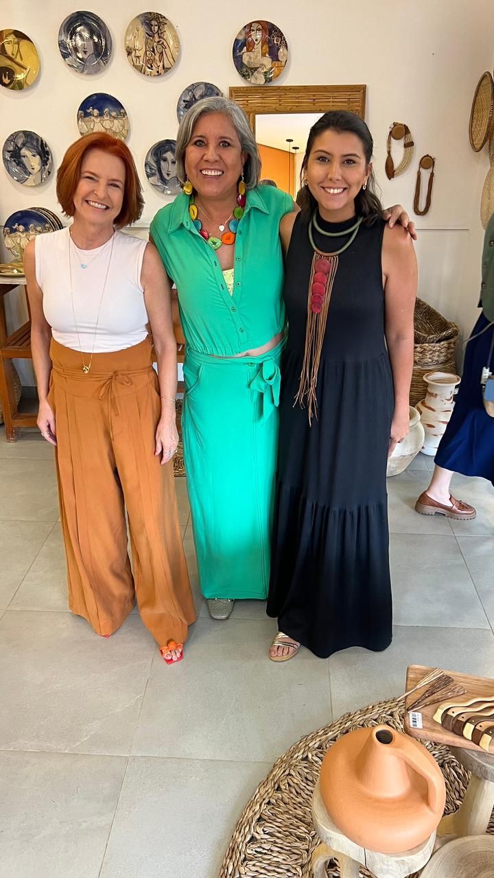Três mulheres estão posando para uma foto em uma sala com pratos na parede.