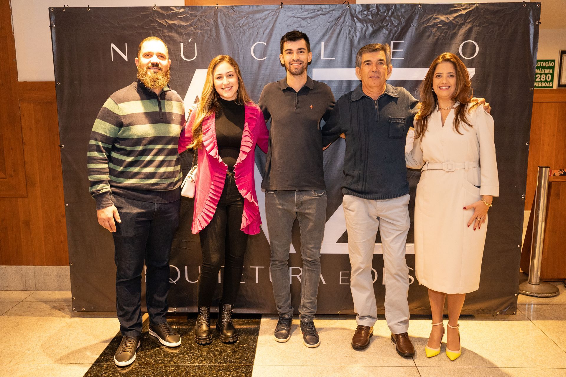 Um grupo de pessoas está posando para uma foto em frente a uma placa.