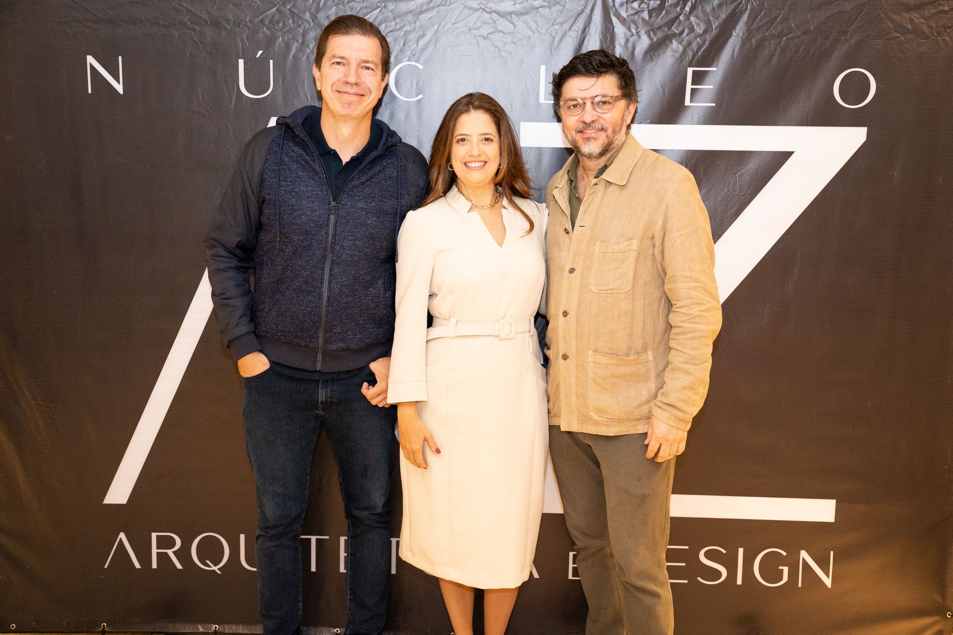 Três pessoas posam para uma foto em frente a uma placa que diz arquitetura design