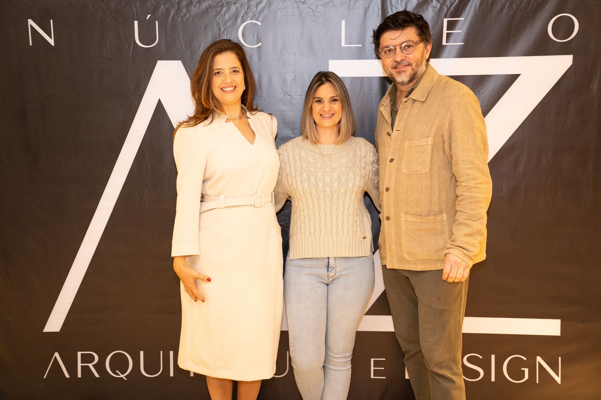 Três pessoas estão posando para uma foto em frente a uma placa.