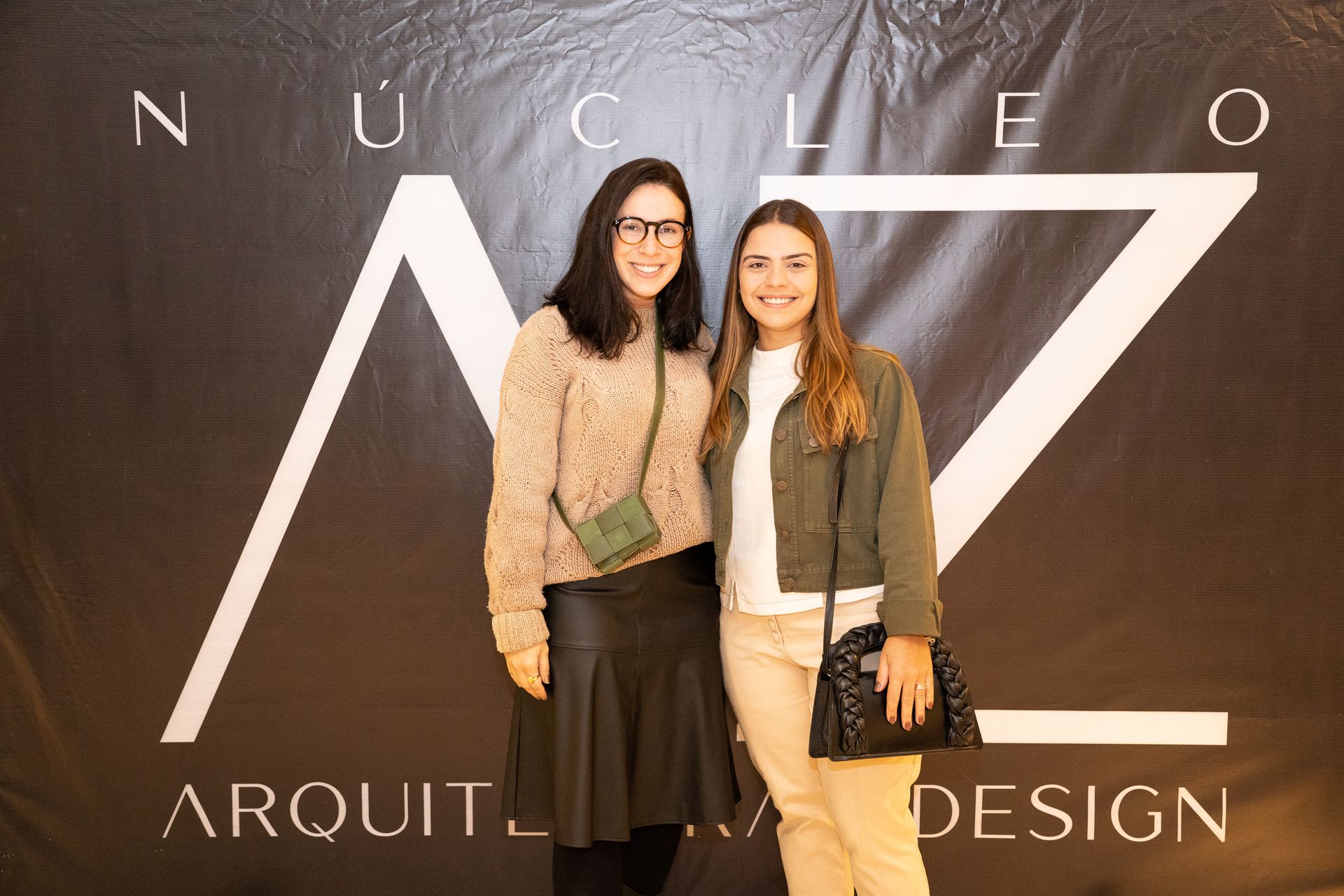Duas mulheres estão posando para uma foto em frente a uma placa que diz arquitetura design.