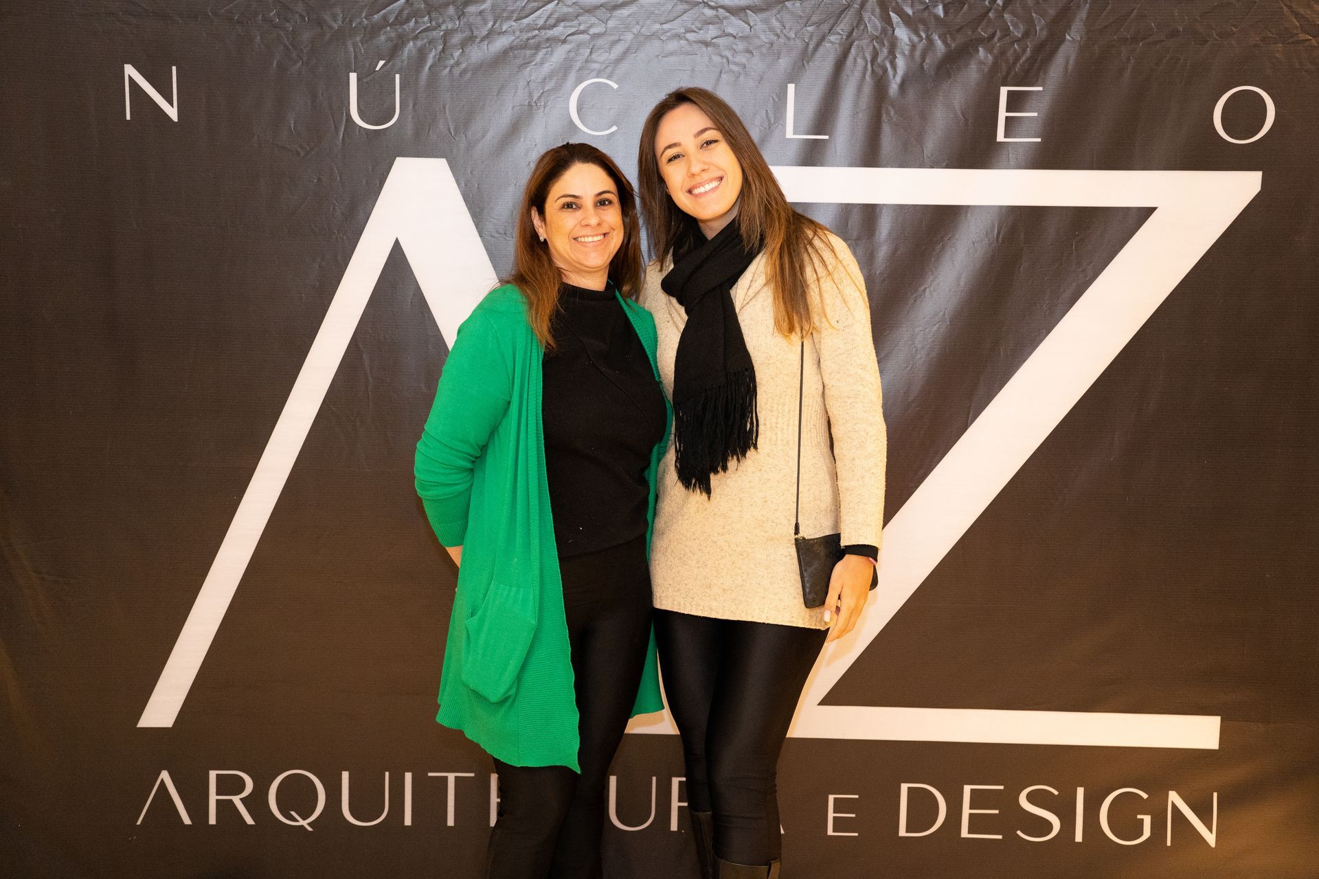 Duas mulheres posam para uma foto em frente a uma placa que diz nucleo