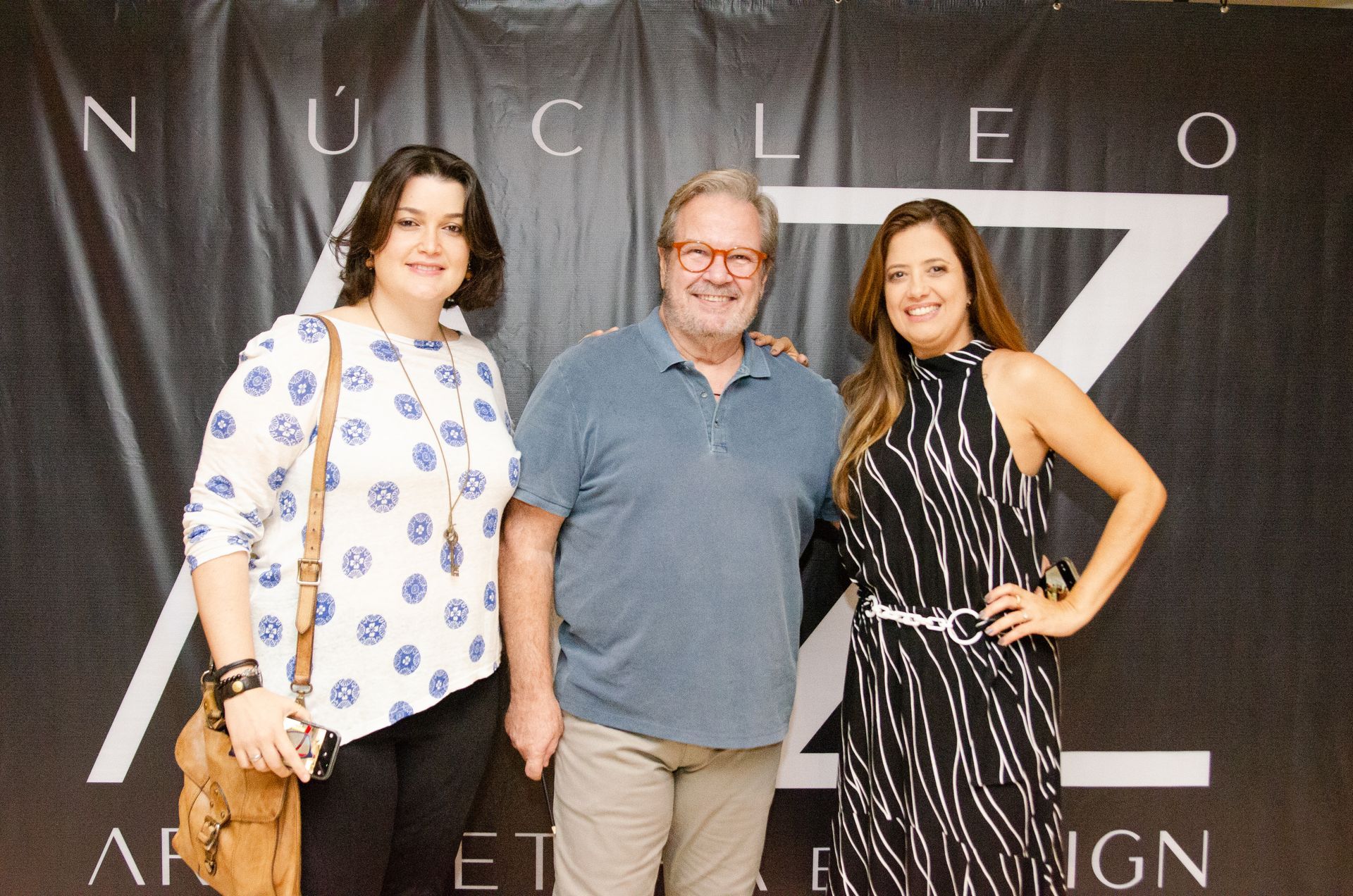 Três pessoas posando para uma foto em frente a uma placa que diz nucleo