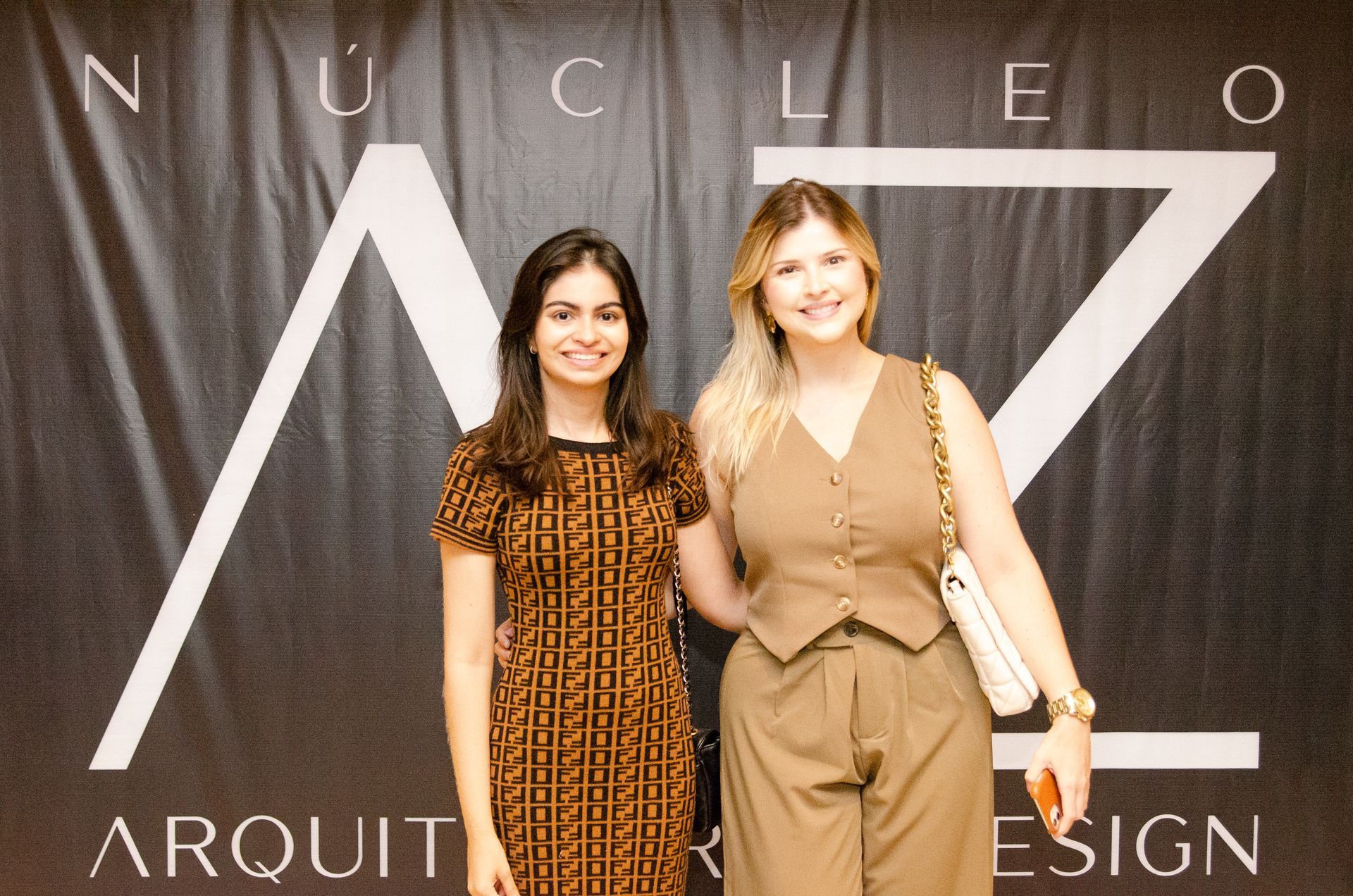 Duas mulheres posam para uma foto em frente a uma placa que diz nucleo arquit design