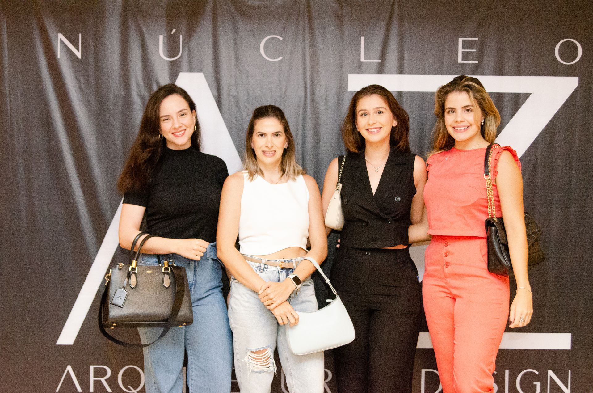 Quatro mulheres estão posando para uma foto em frente a uma placa que diz nucleo