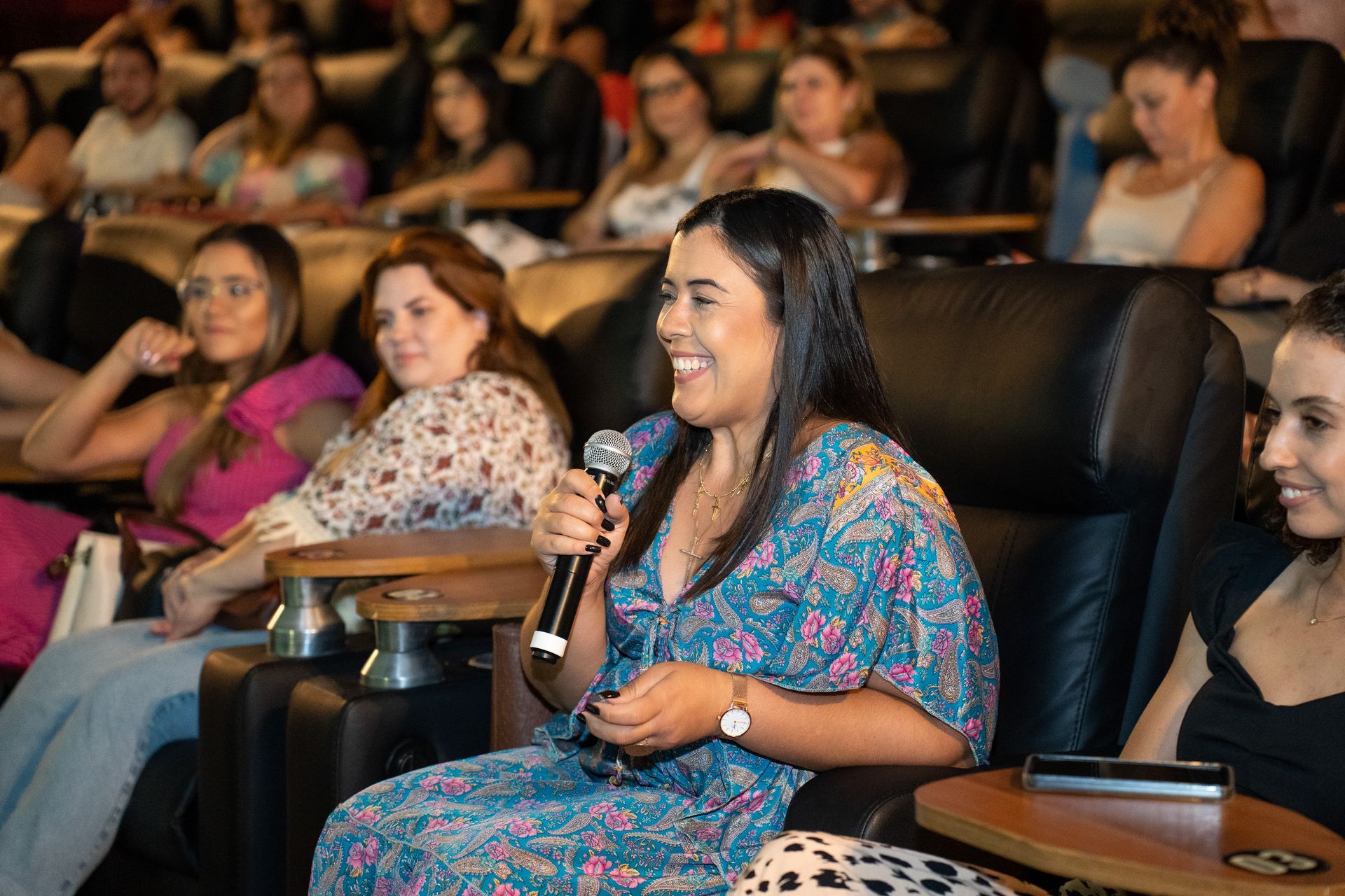Uma mulher segura um microfone enquanto está sentada em um teatro.