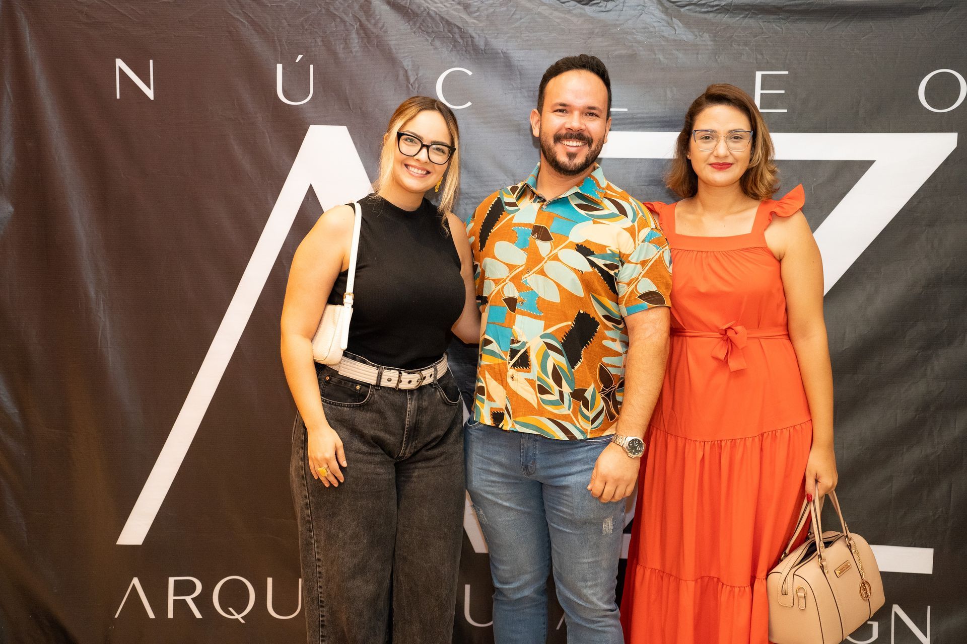 Um homem e duas mulheres estão posando para uma foto em frente a uma placa.