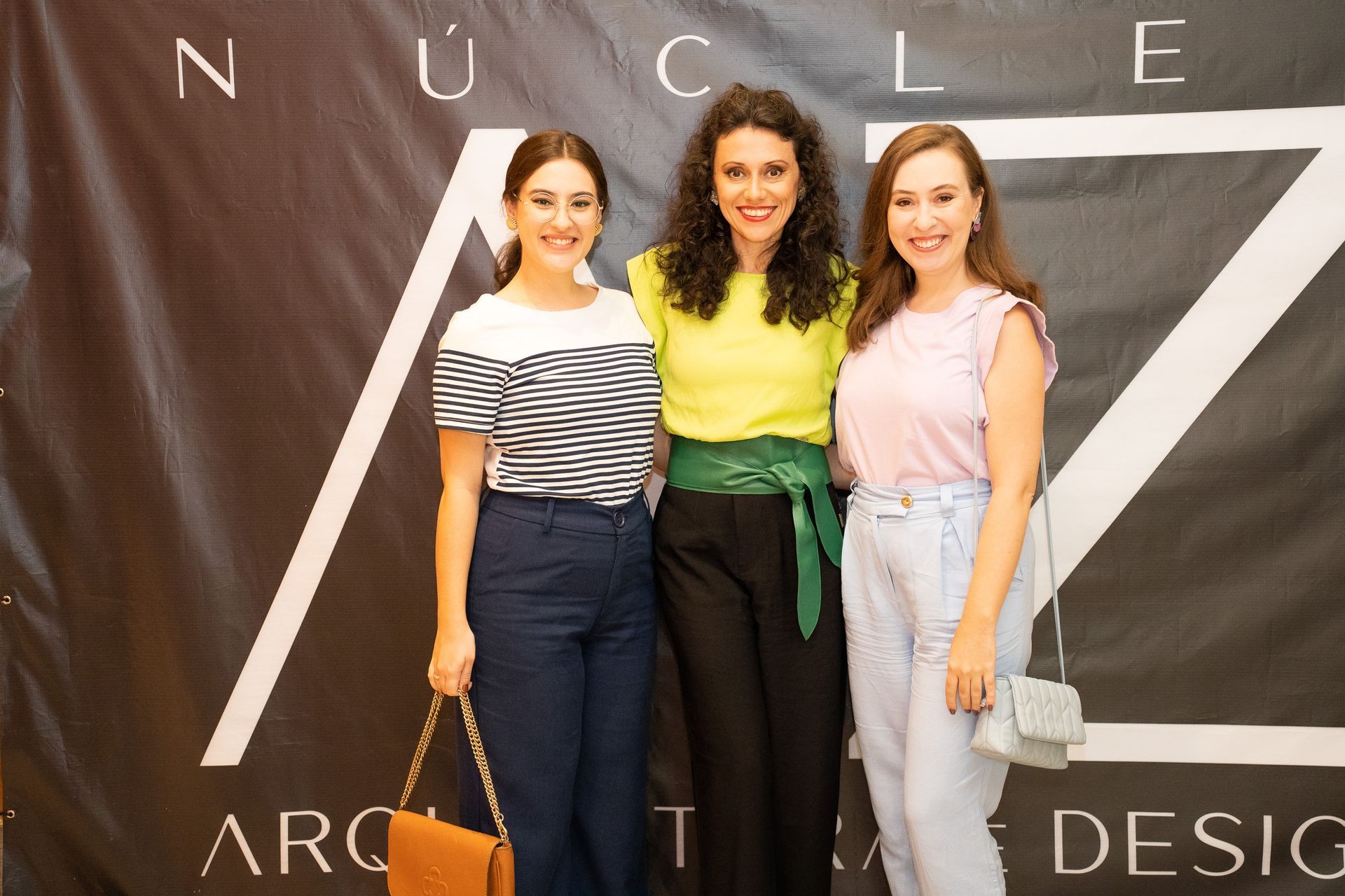 Três mulheres estão posando para uma foto em frente a uma placa.
