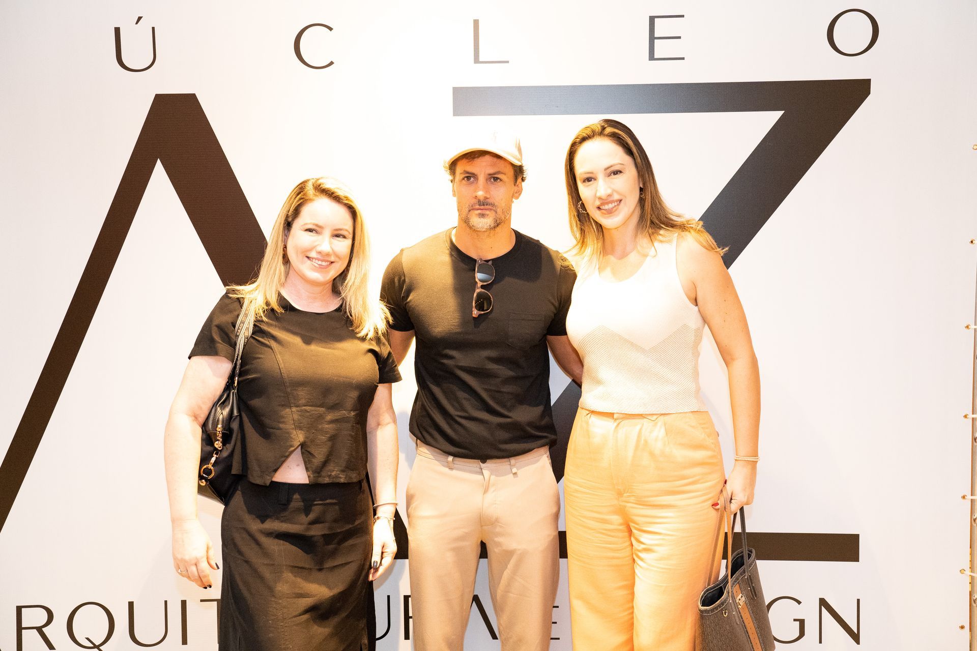 Um homem e duas mulheres estão posando para uma foto em frente a uma placa.