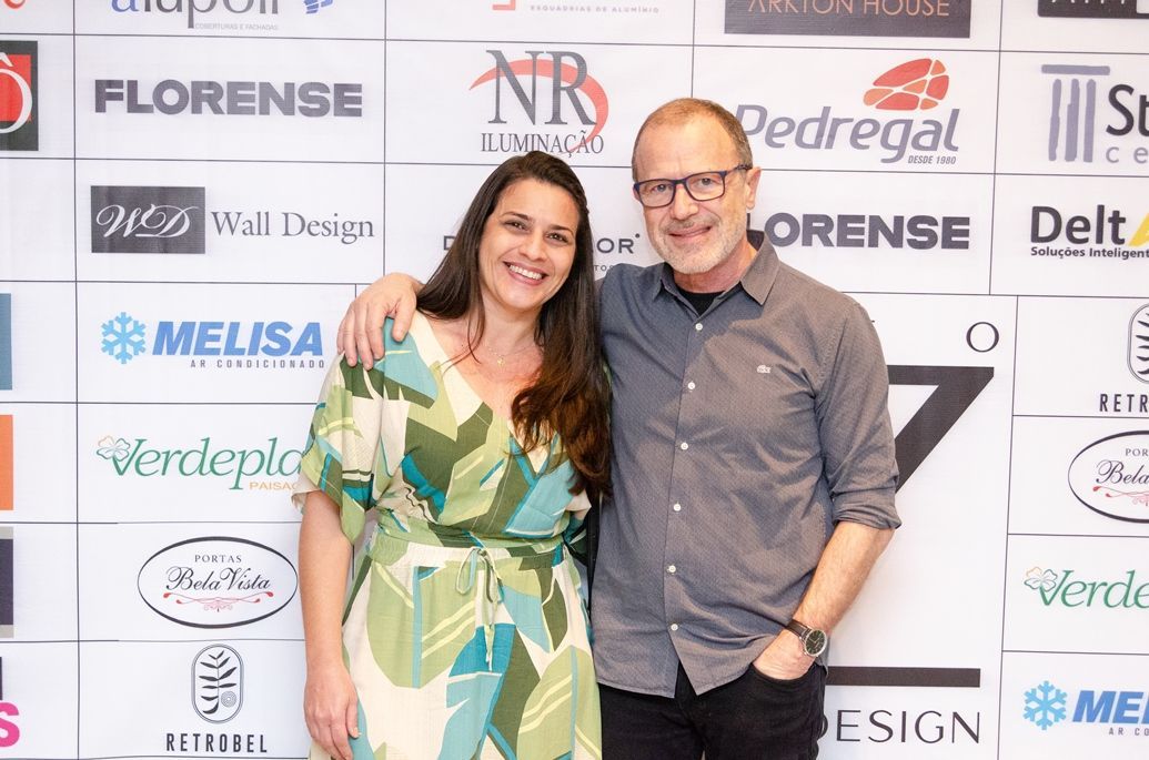Um homem e uma mulher estão posando para uma foto em frente a uma parede com logotipos.