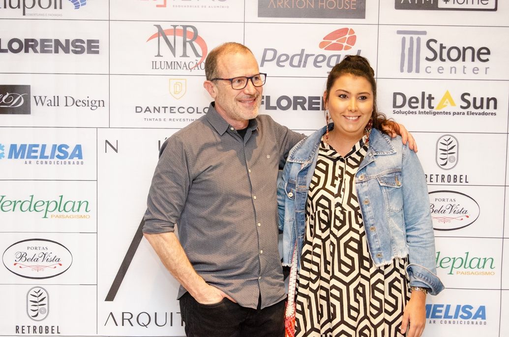 Um homem e uma mulher estão posando para uma foto em frente a uma parede com logotipos.