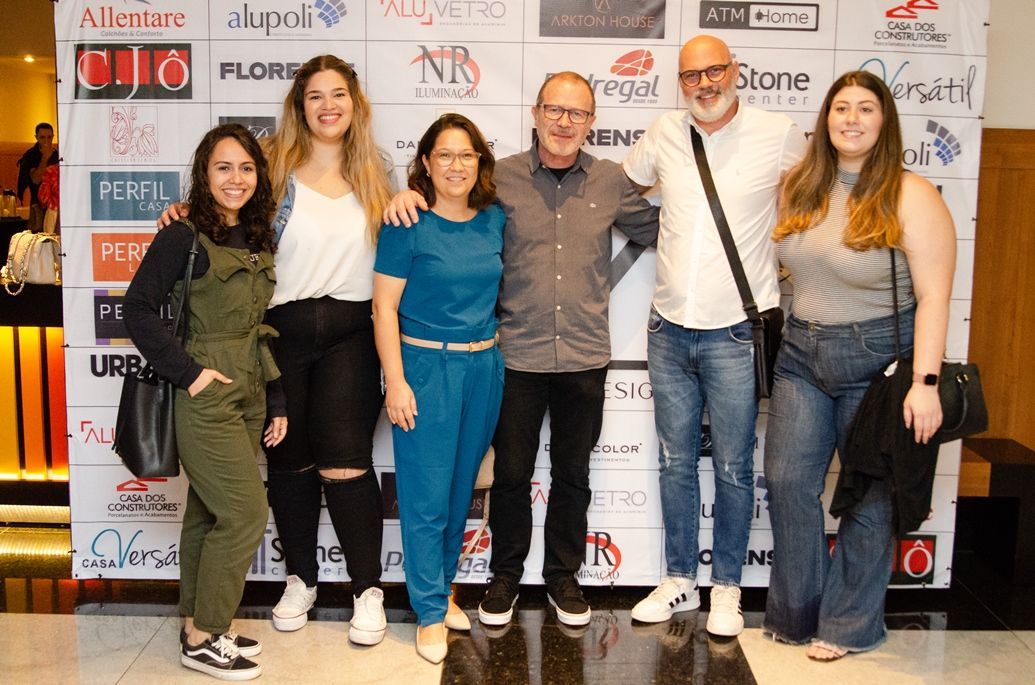 Um grupo de pessoas está posando para uma foto em frente a uma parede com logotipos.