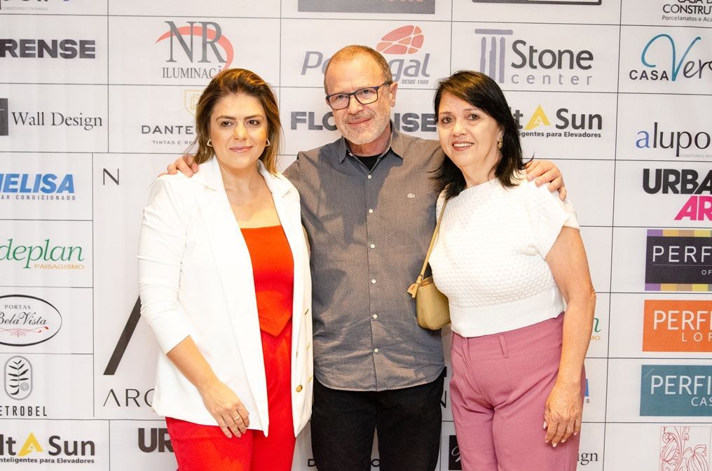 Um homem e duas mulheres estão posando para uma foto em frente a uma parede com logotipos.