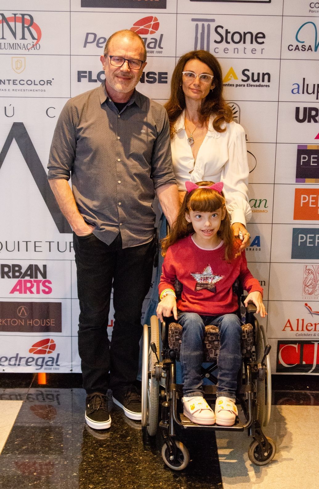 Um homem, uma mulher e uma menina em uma cadeira de rodas estão posando para uma foto.
