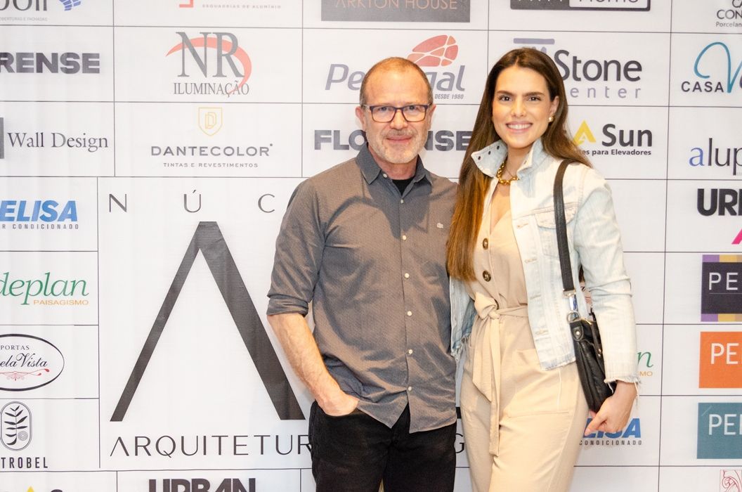 Um homem e uma mulher estão posando para uma foto em frente a uma parede com logotipos.