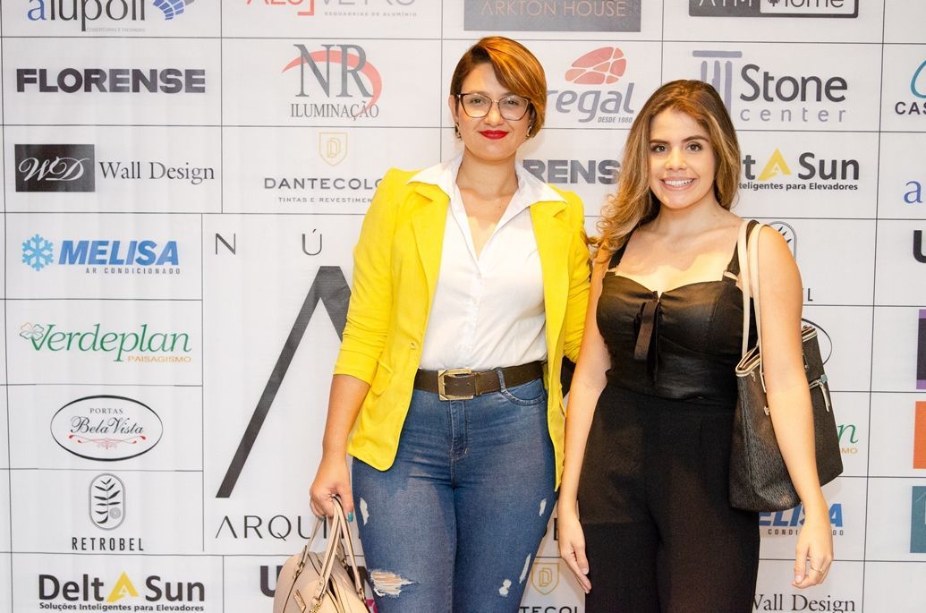 Duas mulheres estão posando para uma foto em frente a uma parede com logotipos.