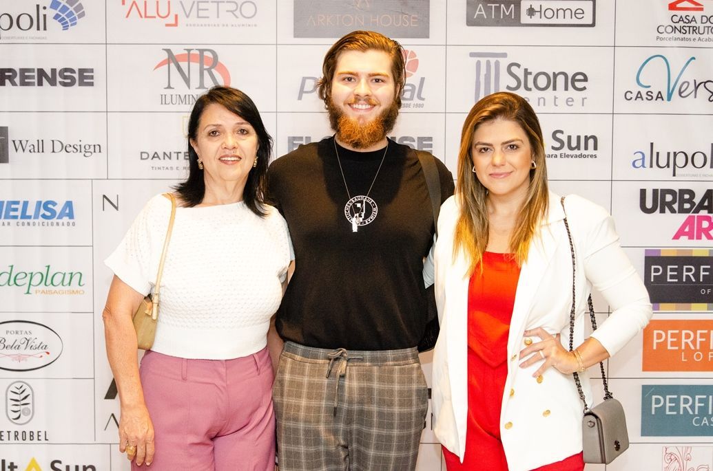 Um homem e duas mulheres estão posando para uma foto em frente a uma parede com logotipos.