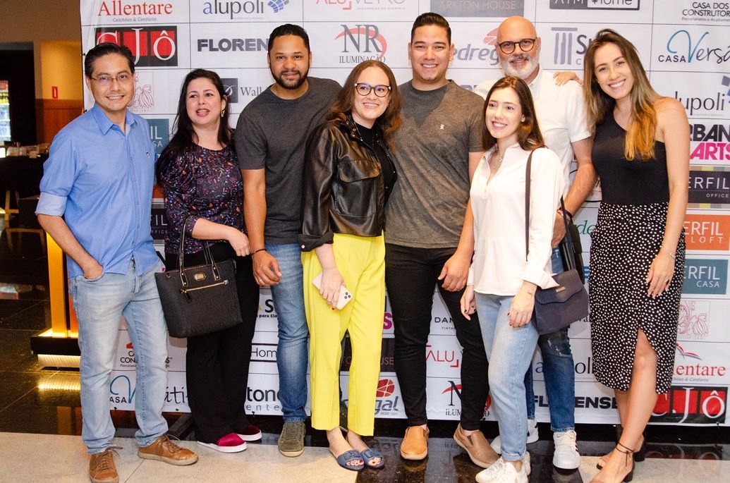 Um grupo de pessoas está posando para uma foto em frente a uma parede com logotipos.