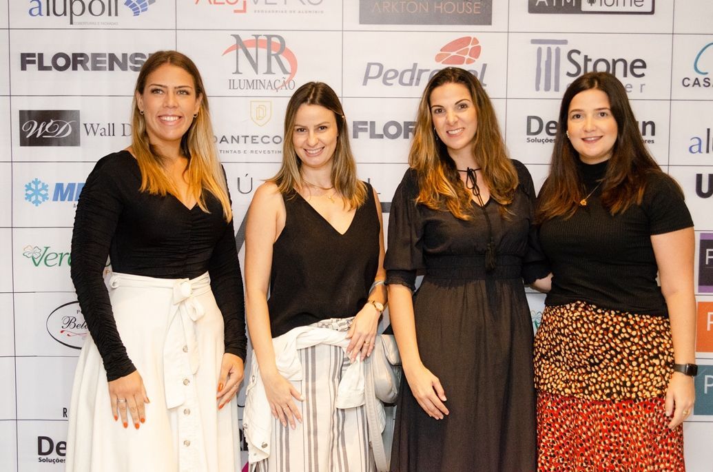 Um grupo de mulheres está posando para uma foto em frente a uma parede com logotipos.
