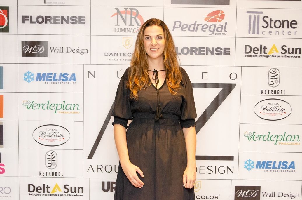 Uma mulher de vestido preto está parada em frente a uma parede de logotipos.