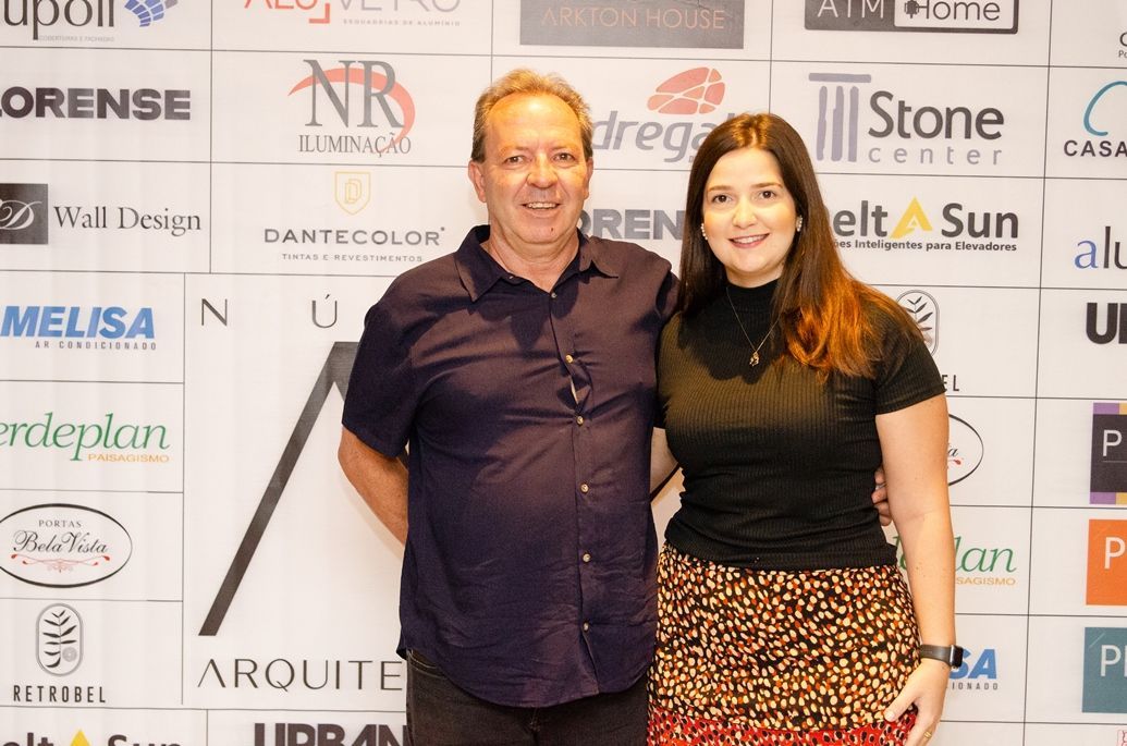 Um homem e uma mulher estão posando para uma foto em frente a uma parede com logotipos.