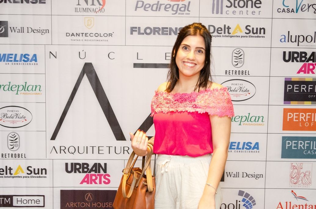 Uma mulher com uma blusa rosa está parada em frente a uma parede de logotipos