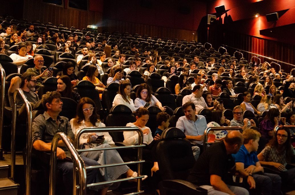 Uma grande multidão de pessoas está sentada em um cinema assistindo a um filme.
