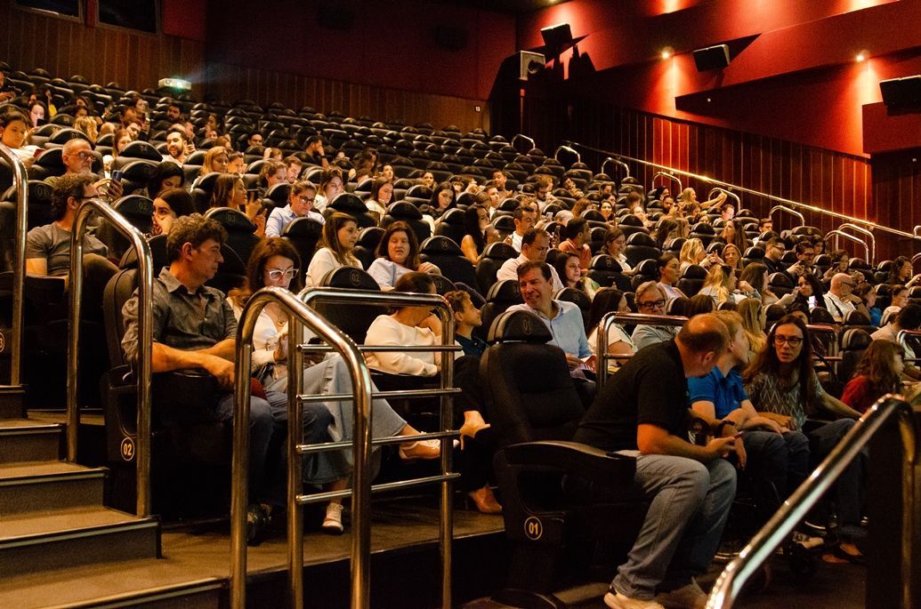 Uma grande multidão de pessoas está sentada em um cinema assistindo a um filme.