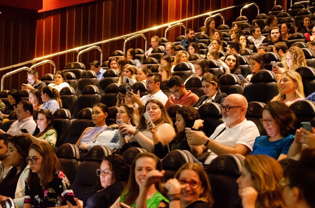 Um grande grupo de pessoas está sentado em um cinema assistindo a um filme.
