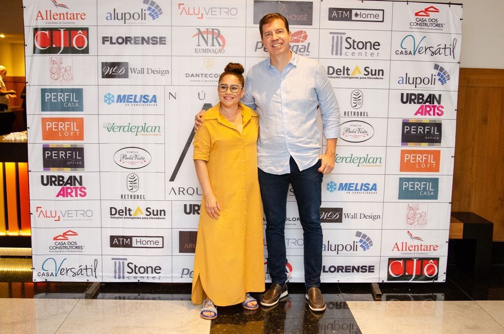 Um homem e uma mulher estão posando para uma foto em frente a uma parede com logotipos.