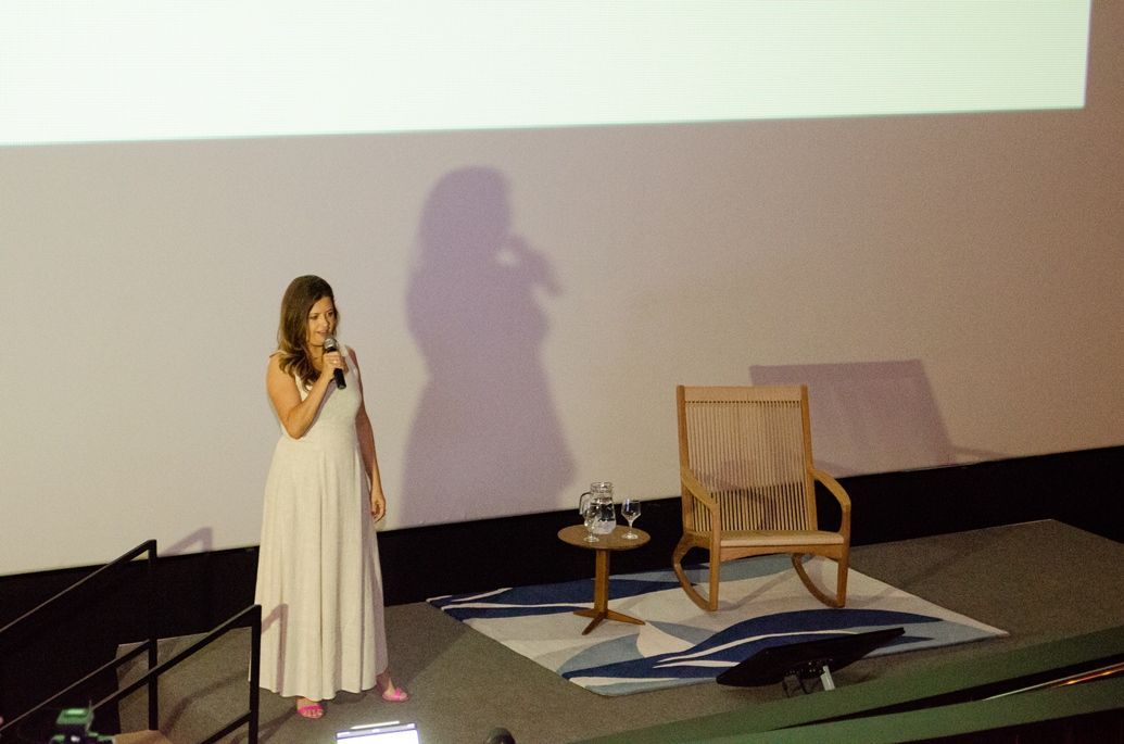 Uma mulher de vestido branco está de pé no palco segurando um microfone.