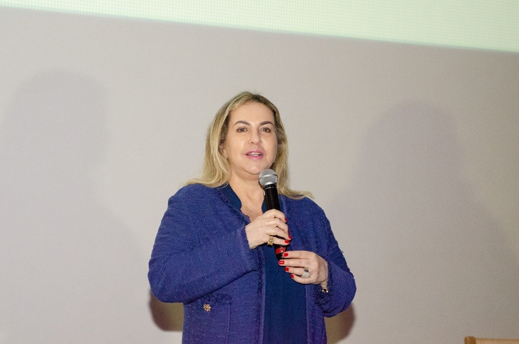 Uma mulher de jaqueta azul está falando em um microfone.