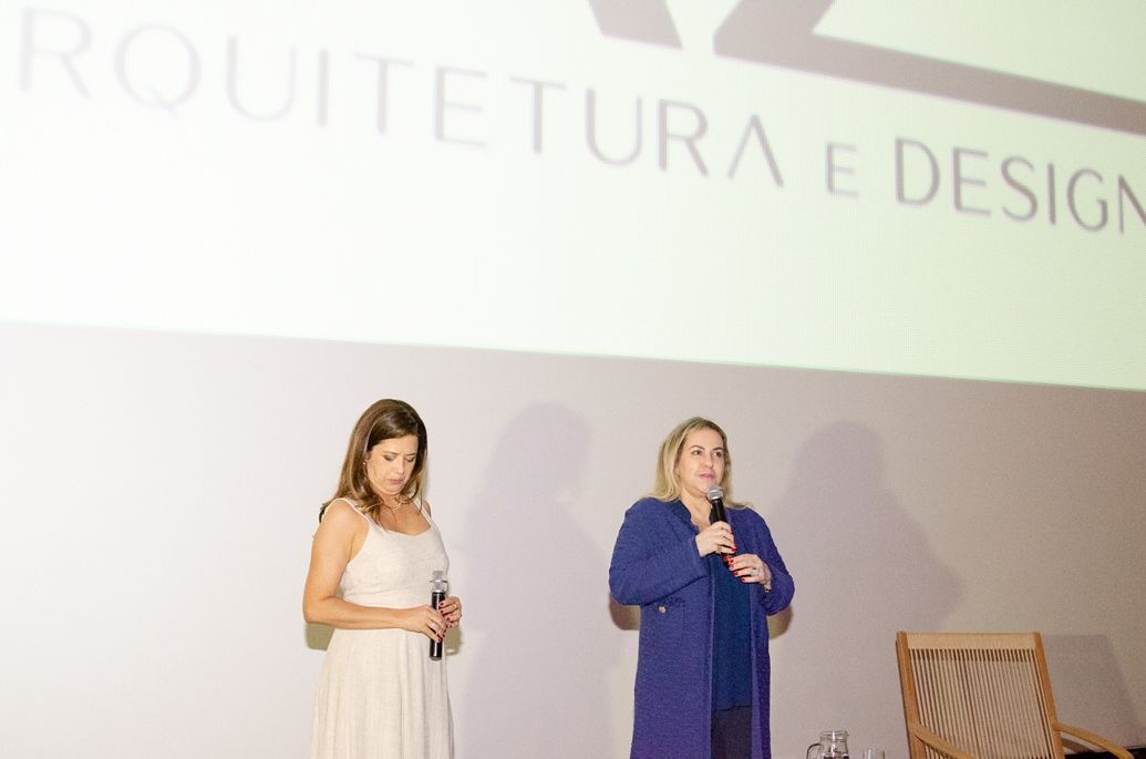 Duas mulheres estão em pé em frente a uma tela de projeção que diz
