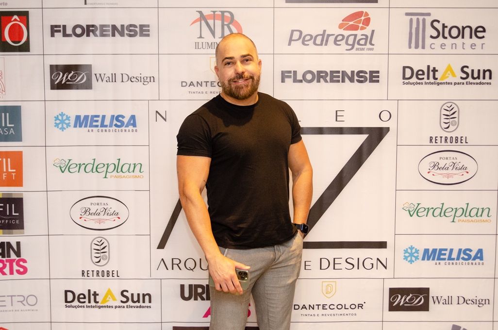 Um homem de camisa preta está parado em frente a uma parede de logotipos