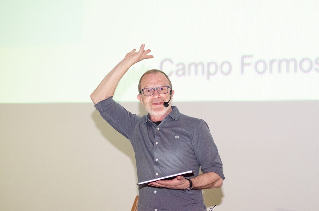 Um homem usando óculos e um microfone está segurando um tablet e fazendo uma apresentação.