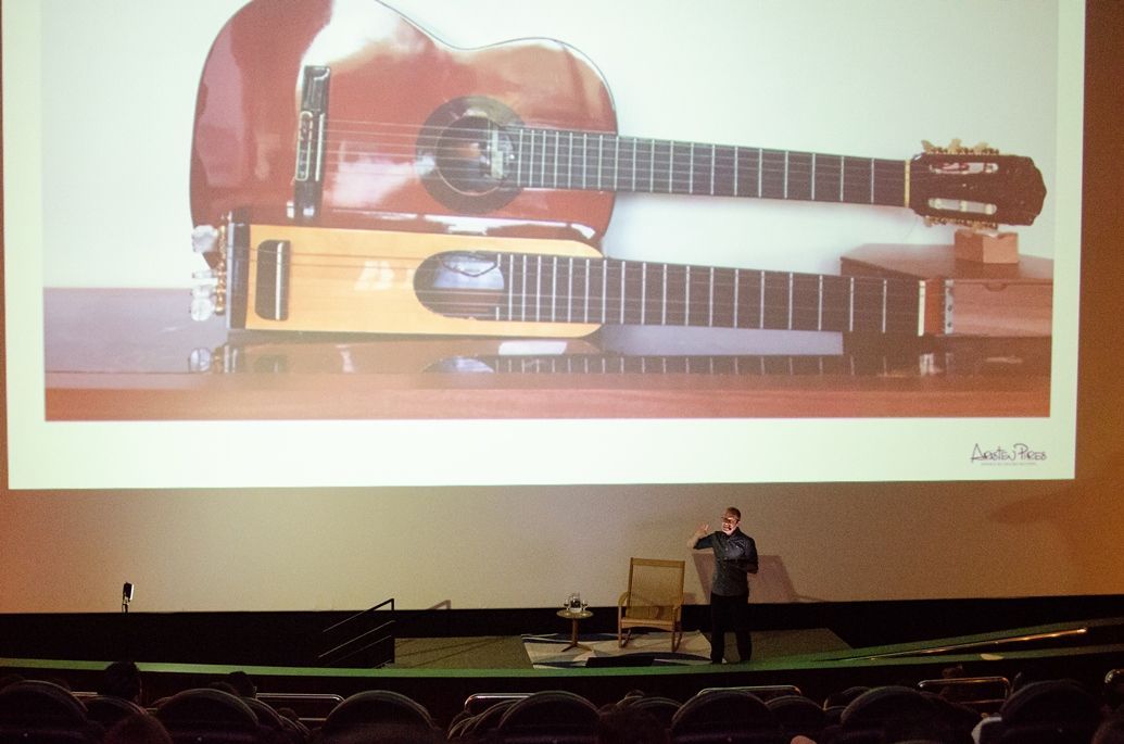Um homem está em frente a uma tela grande com uma imagem de guitarras nela