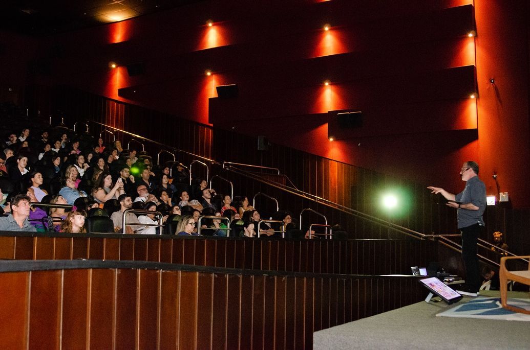 Um homem está em pé em um palco em frente a uma multidão de pessoas em um auditório.