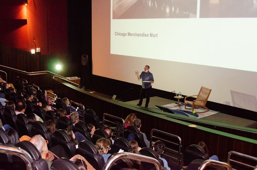 Um homem está fazendo uma apresentação em frente a uma tela grande em um teatro