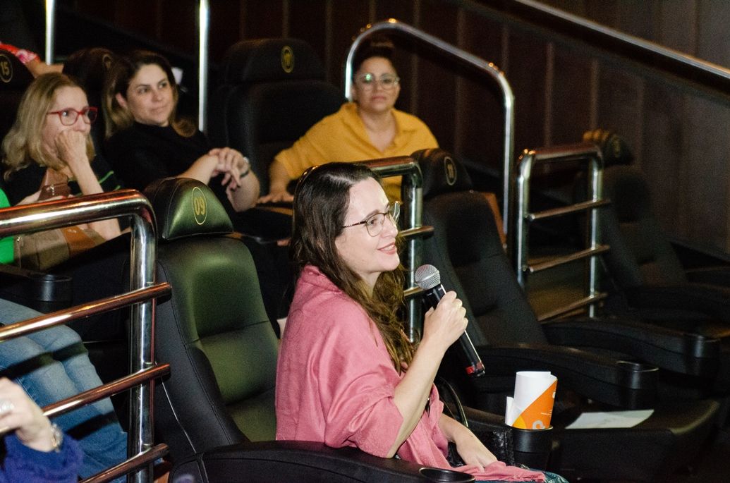 Uma mulher segura um microfone enquanto está sentada em um teatro.