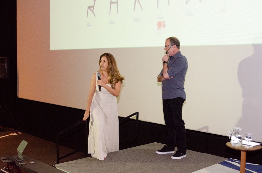 Um homem e uma mulher estão em pé no palco em frente a uma tela grande.