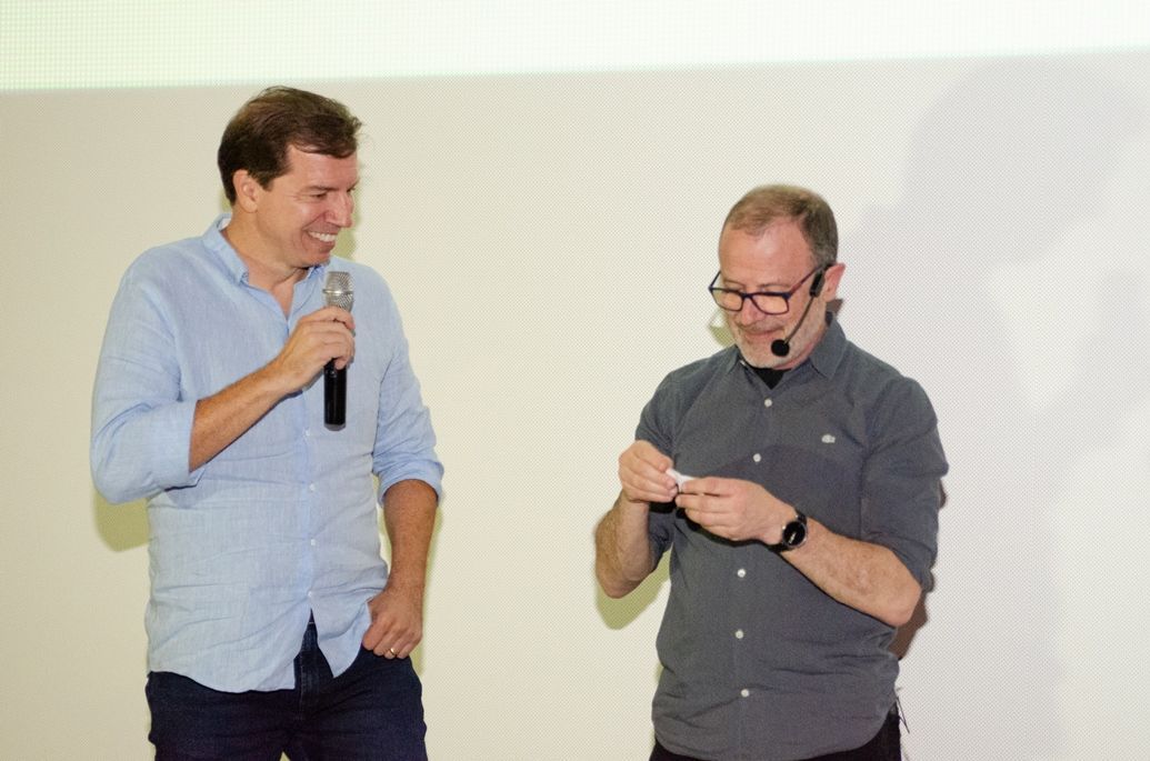 Dois homens estão de pé, um ao lado do outro, falando em microfones.